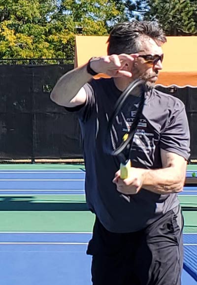 John Hart hitting a back-hand shot while playing tennis.