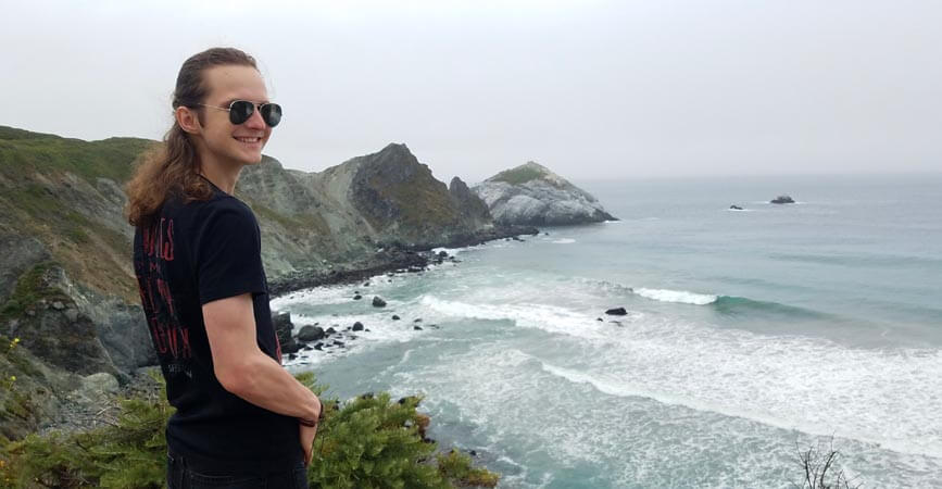 Rob Reichert standing on a lush cliff that overlooks the ocean on an overcast day.